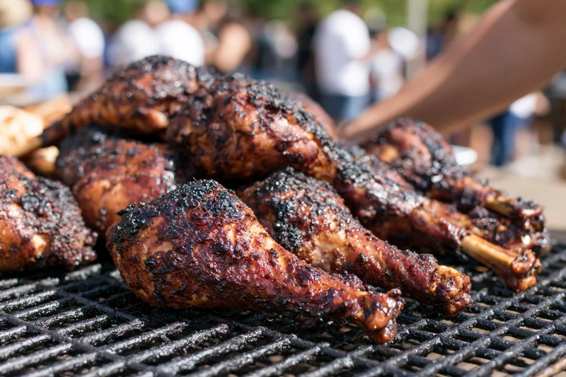 Smoked turkey legs piled on a grill at an outdoor cookout