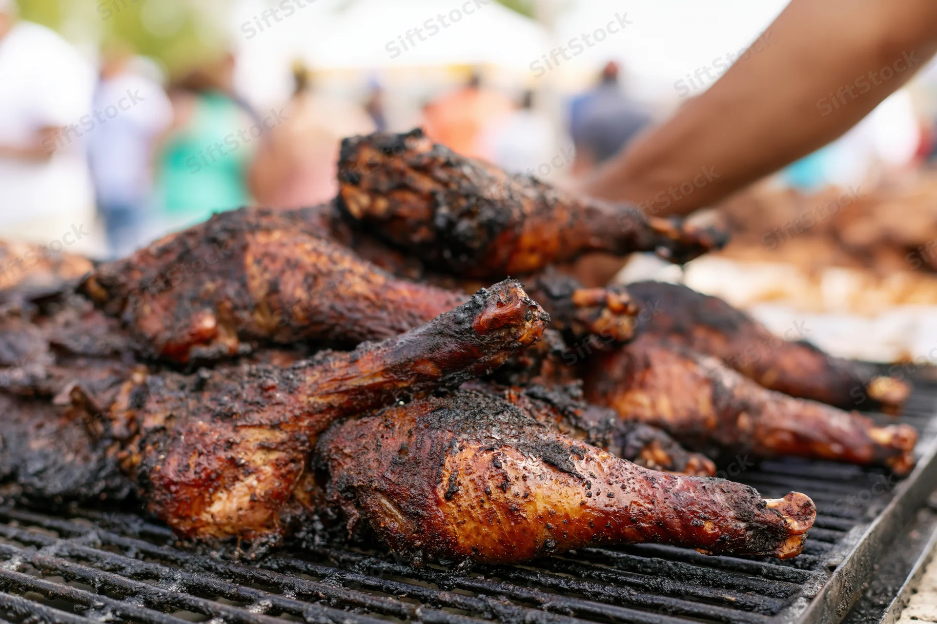 Grilled turkey legs piled on a barbecue grill at an outdoor food market