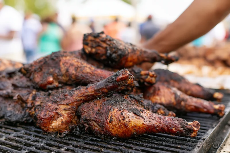 Grilled turkey legs piled on a barbecue grill at an outdoor food market