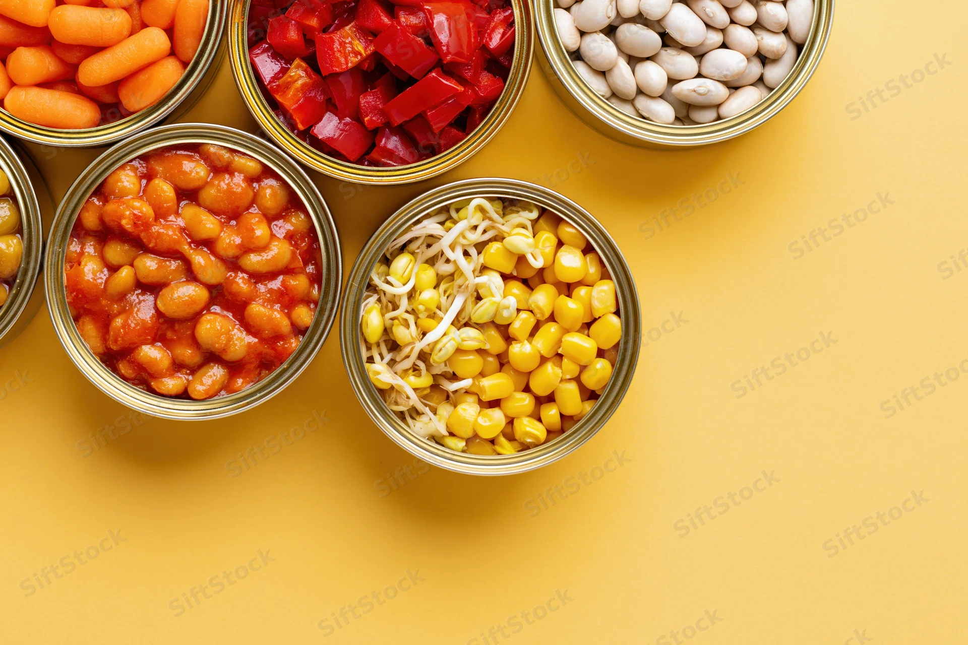 Open tin cans filled with various preserved vegetables arranged on a yellow surface