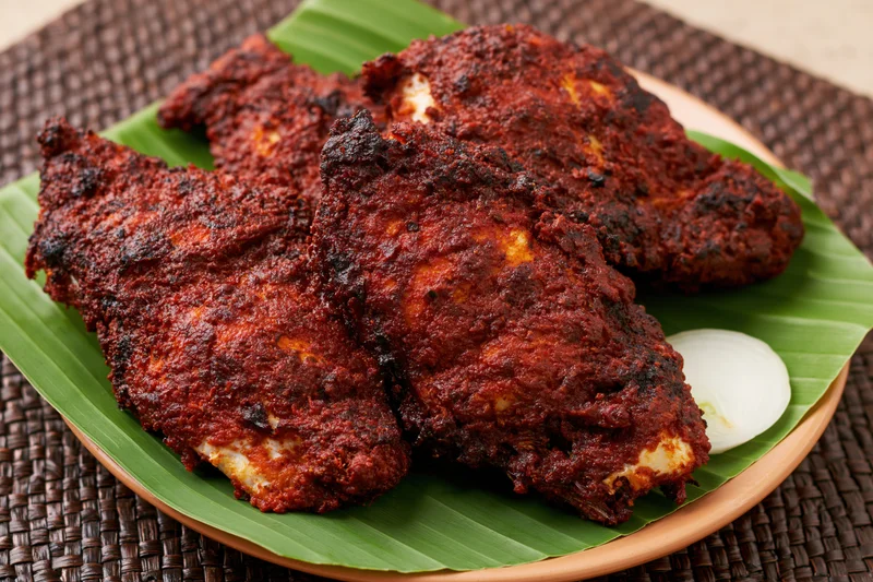Deep-fried spiced fish pieces on a banana leaf-lined plate with onion slice
