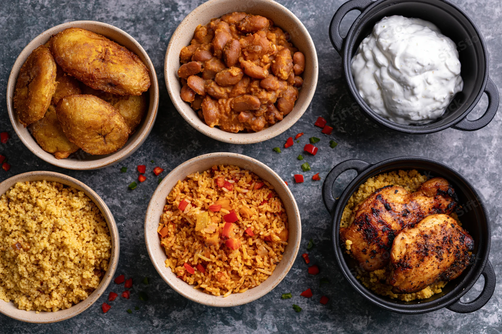 Six bowls of west african food arranged on dark slate surface