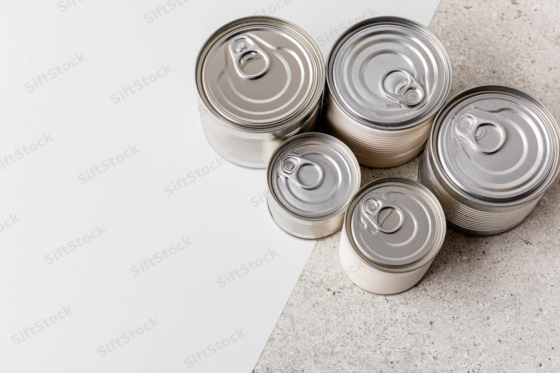 Six unlabeled tin cans of varying sizes arranged on a white and concrete surface