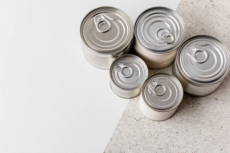 Six unlabeled tin cans of varying sizes arranged on a white and concrete surface