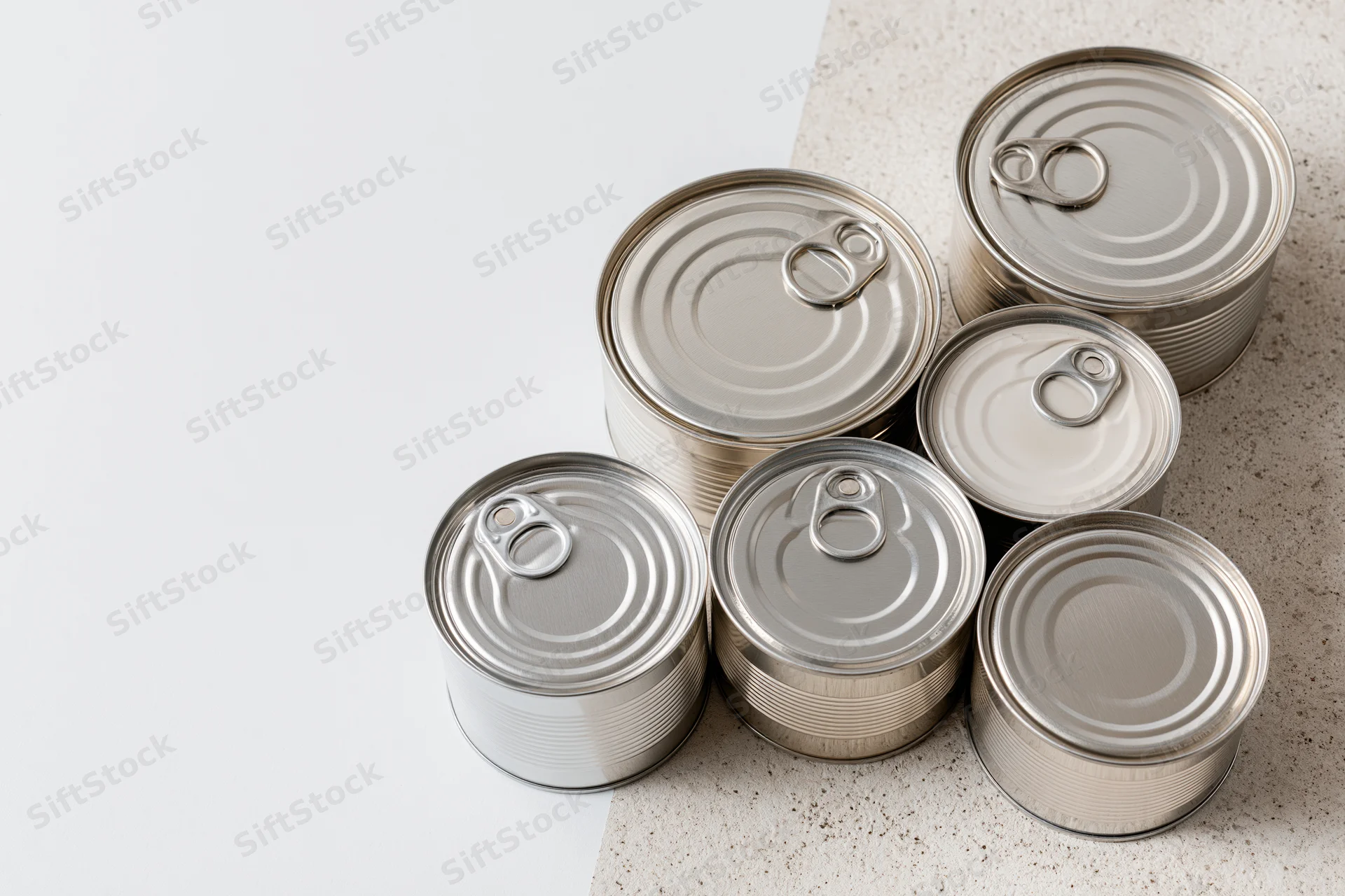Six unlabeled tin cans of varying sizes arranged on a speckled surface with white copyspace to the left