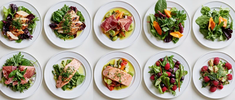 Ten plates of assorted salads and protein dishes arranged in two rows on a white surface