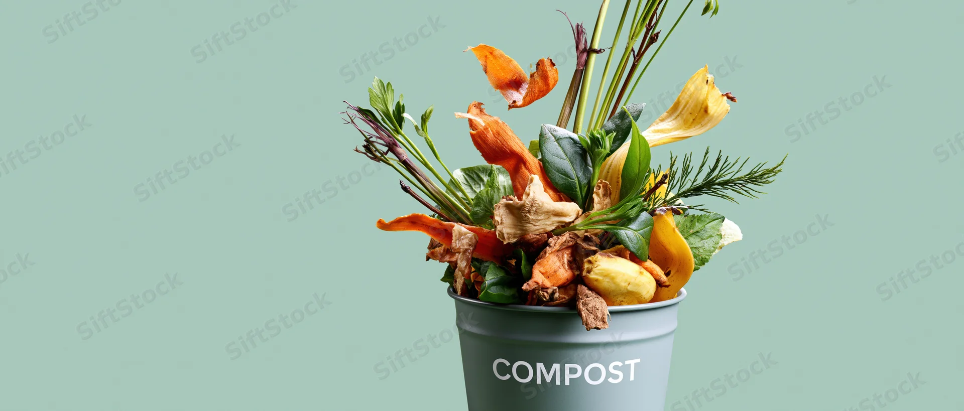 Grey metal bucket labeled compost overflowing with vegetable scraps and plant waste