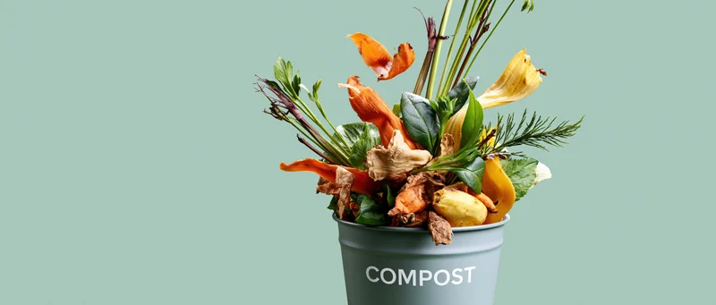 Grey metal bucket labeled compost overflowing with vegetable scraps and plant waste
