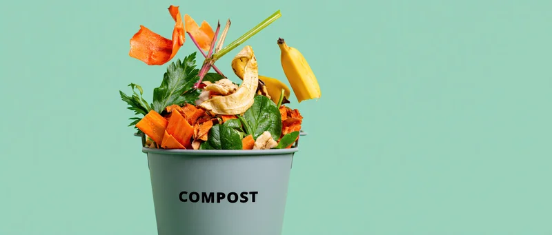 Grey metal bucket labeled compost overflowing with vegetable scraps against a light green background