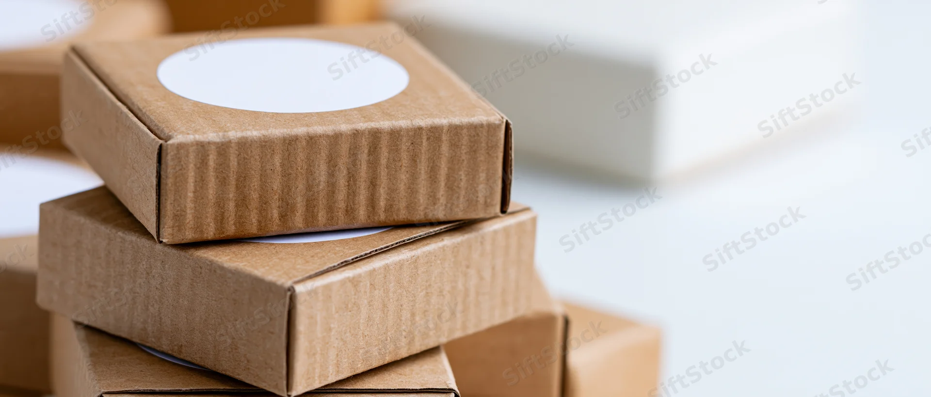 Stack of small kraft cardboard boxes with white circular stickers on a light surface