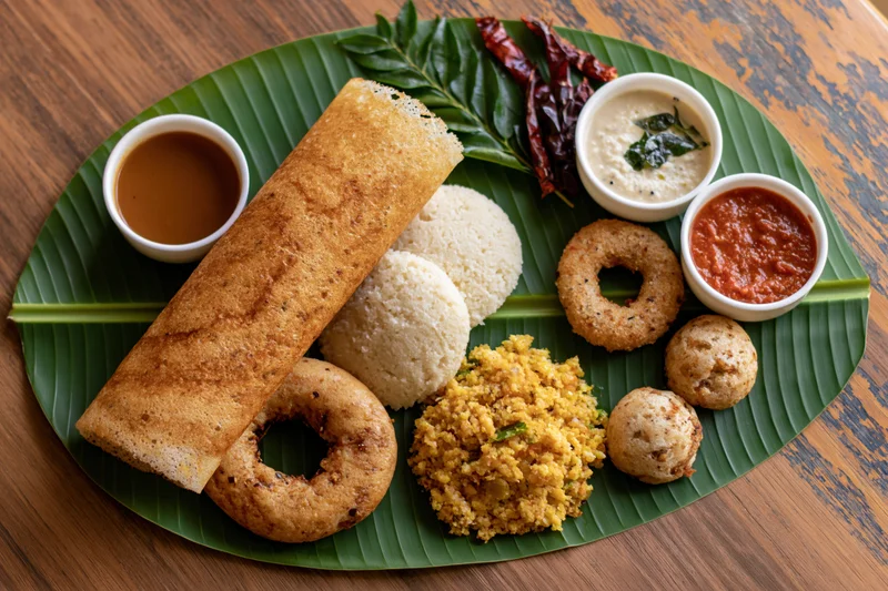 South indian breakfast spread arranged on a large fresh banana leaf with dosa, idli, vada, sambar, and chutney on a