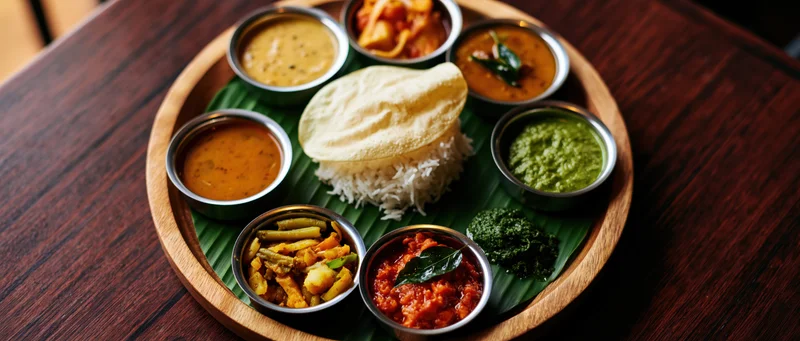 South indian thali meal served on banana leaf with rice, dosa, curries and chutneys on wooden tray