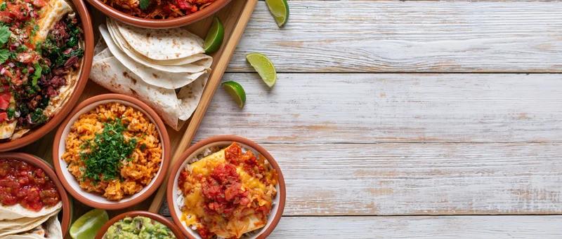 Mexican food dishes arranged along left edge of white wooden table with copyspace on right