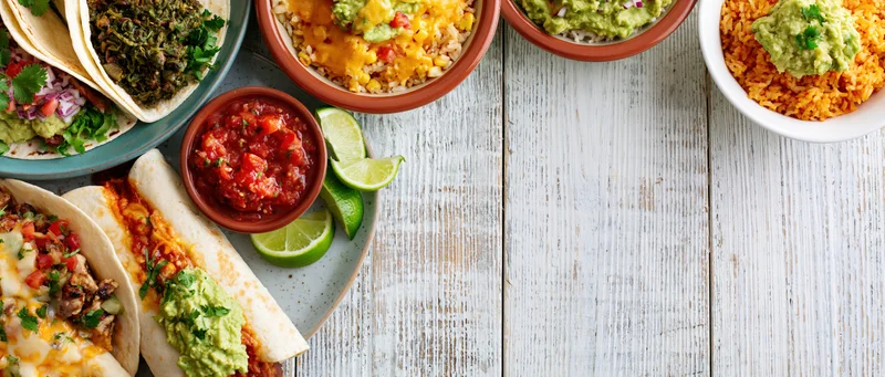 Mexican food dishes arranged along the left edge of a white wooden table with copyspace on the right