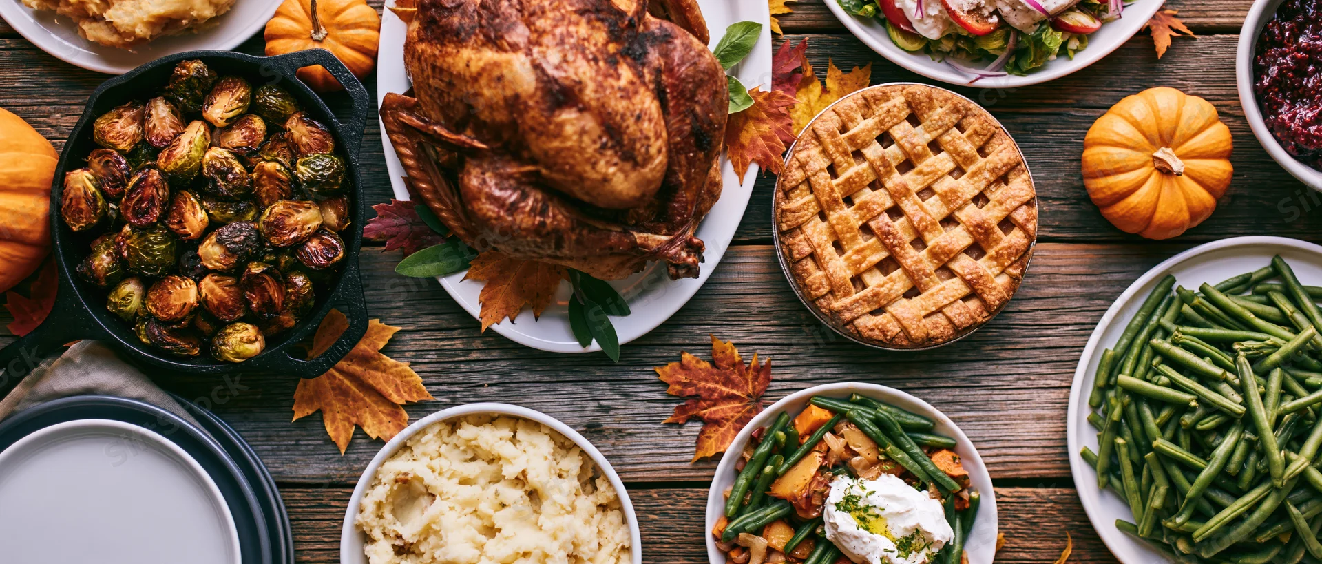 Roasted turkey and Thanksgiving dishes arranged on a weathered wooden farmhouse table with autumn leaves and pumpkins