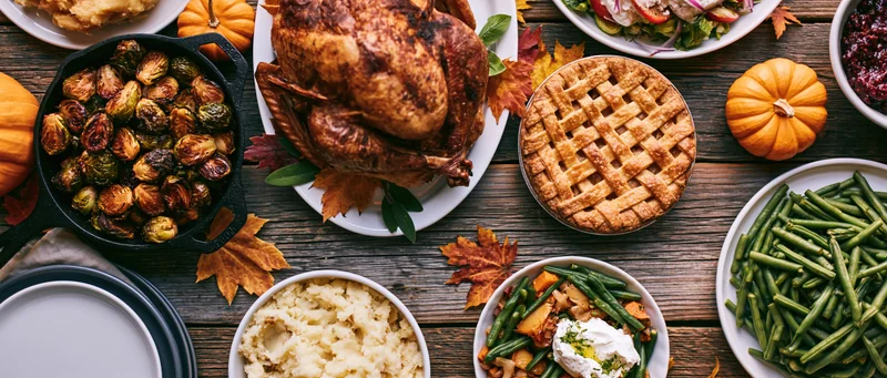 Roasted turkey and Thanksgiving dishes arranged on a weathered wooden farmhouse table with autumn leaves and pumpkins