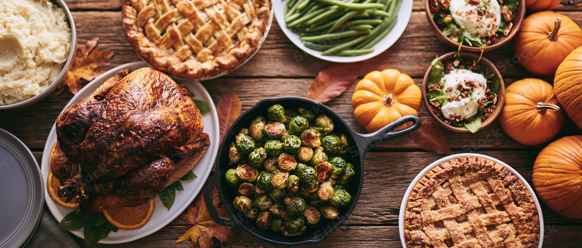 Thanksgiving feast with roasted turkey, pies, and vegetables arranged on a rustic wooden farmhouse table