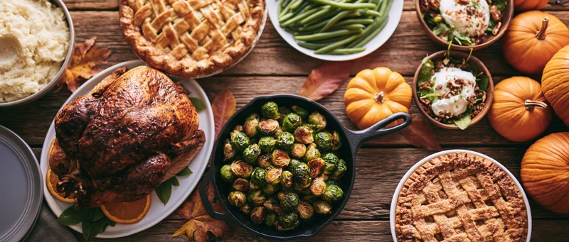 Thanksgiving feast with roasted turkey, pies, and vegetables arranged on a rustic wooden farmhouse table