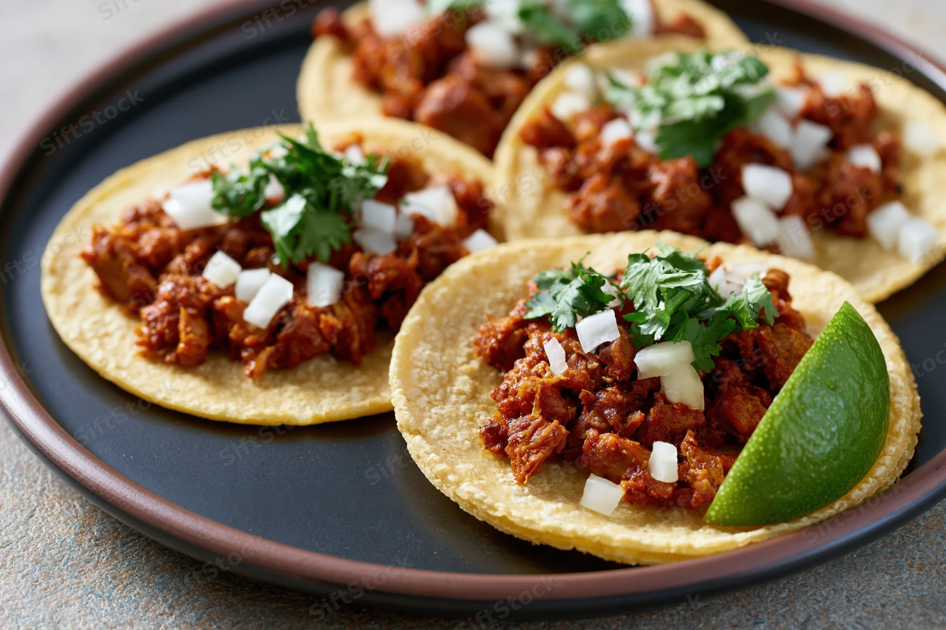 Al pastor tacos on small corn tortillas topped with diced onion, cilantro, and lime wedge on a black plate
