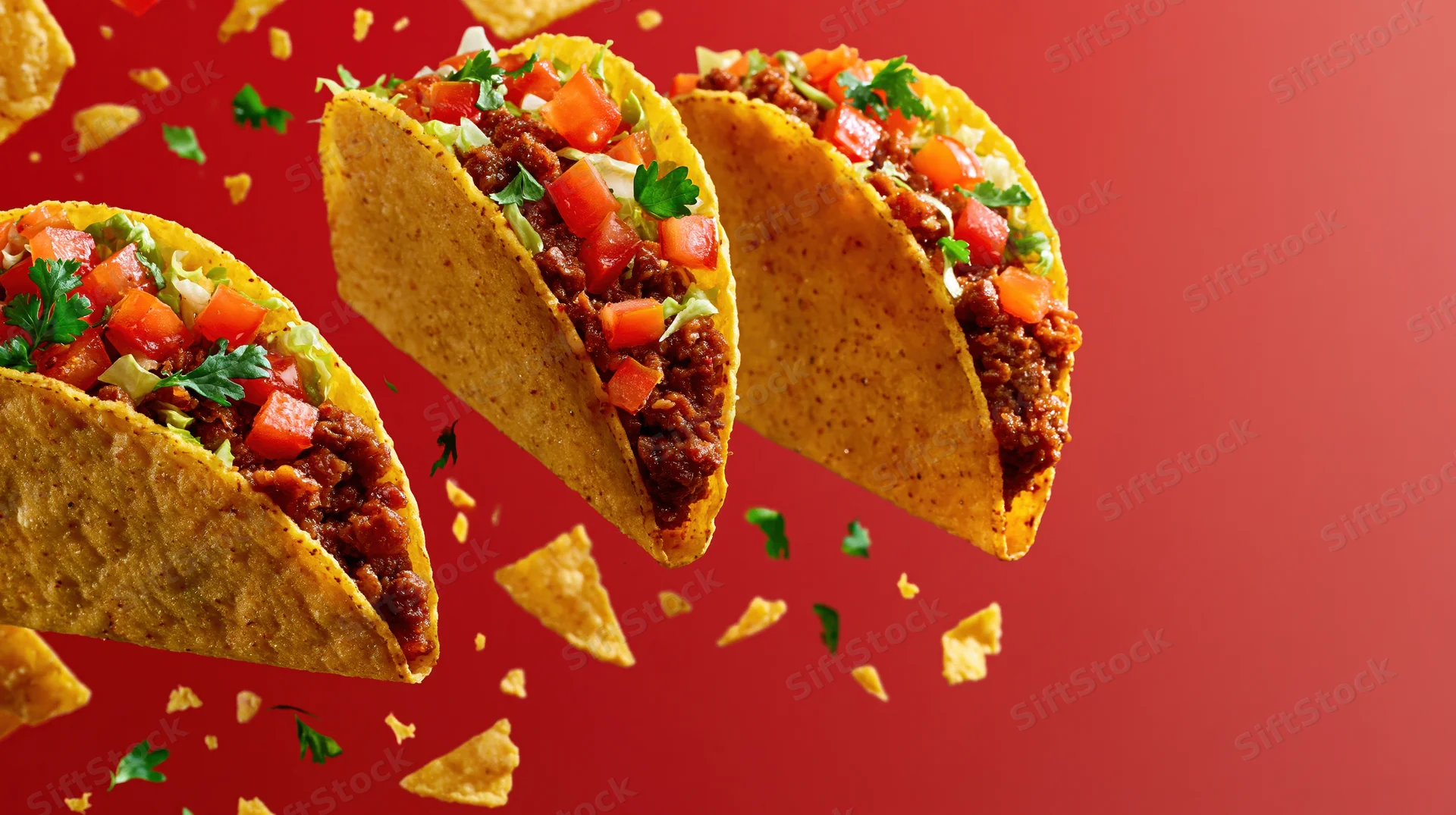 Three crispy corn tacos filled with seasoned ground beef and topped with diced tomatoes and cilantro floating against a red background