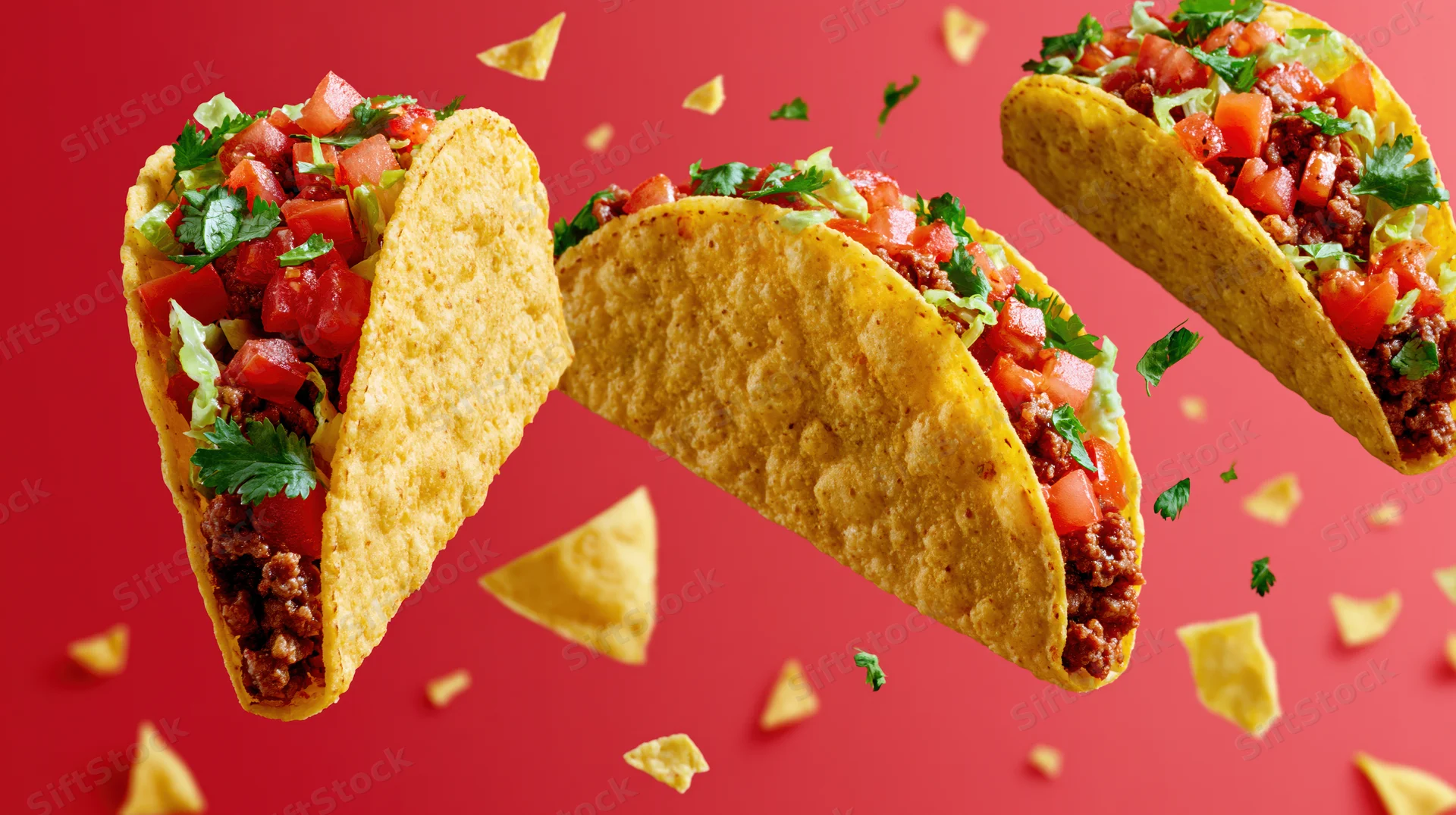 Three crispy corn tacos filled with seasoned ground beef and fresh toppings floating against a red background