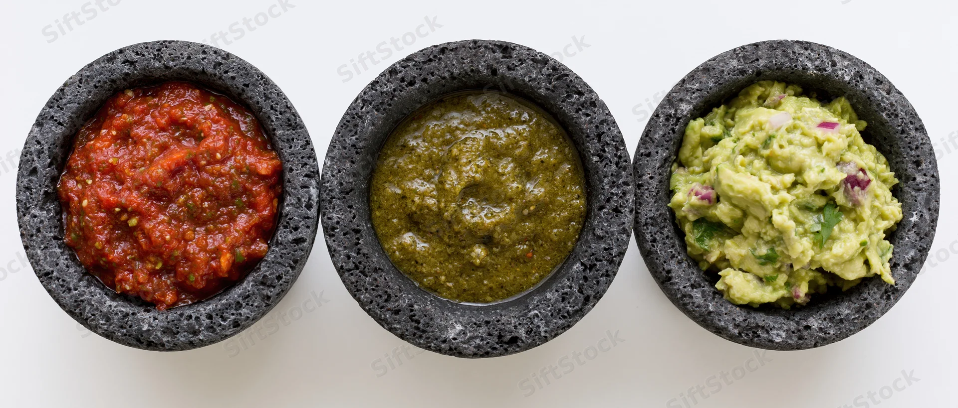 Three molcajetes filled with red salsa, green salsa, and guacamole arranged in a row on a white surface