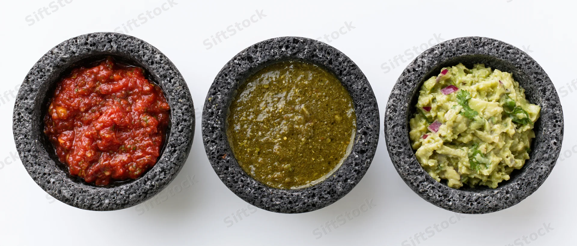 Three dark gray volcanic stone molcajetes each holding a different salsa arranged in a row on a white surface