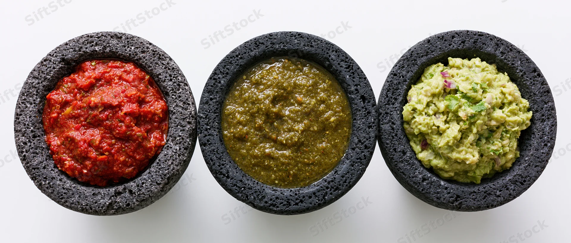 Three molcajetes filled with red salsa, green salsa, and guacamole arranged in a row on a white surface