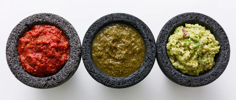 Three molcajetes filled with red salsa, green salsa, and guacamole arranged in a row on a white surface