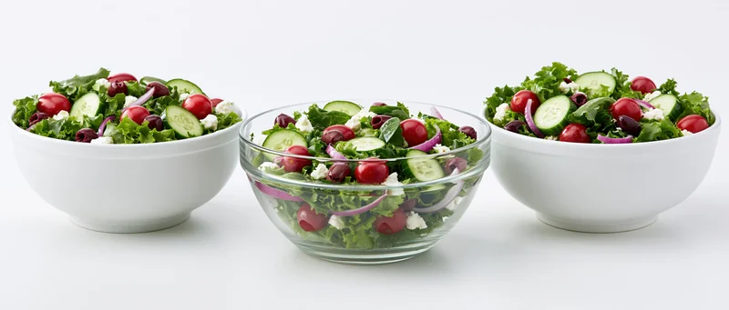 Three fresh garden salads in white and glass bowls arranged side by side on a white surface