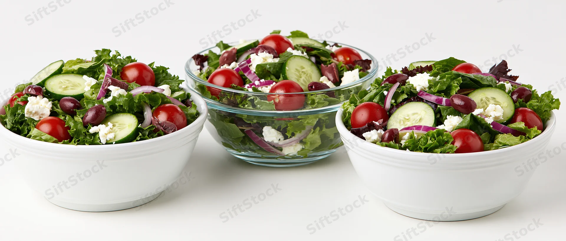 Three fresh garden salads in white and glass bowls arranged side by side on a white surface