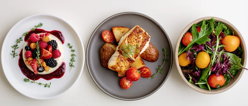 Three restaurant dishes arranged side by side on a white surface, featuring a berry dessert, grilled fish with potatoes, and a mixed salad with tomatoes and greens
