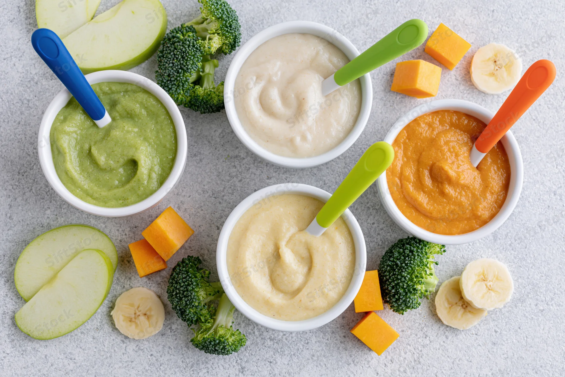 Four bowls of baby food puree with vegetables and fruits arranged on a countertop