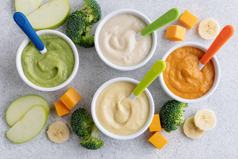 Four bowls of baby food puree with vegetables and fruits arranged on a countertop