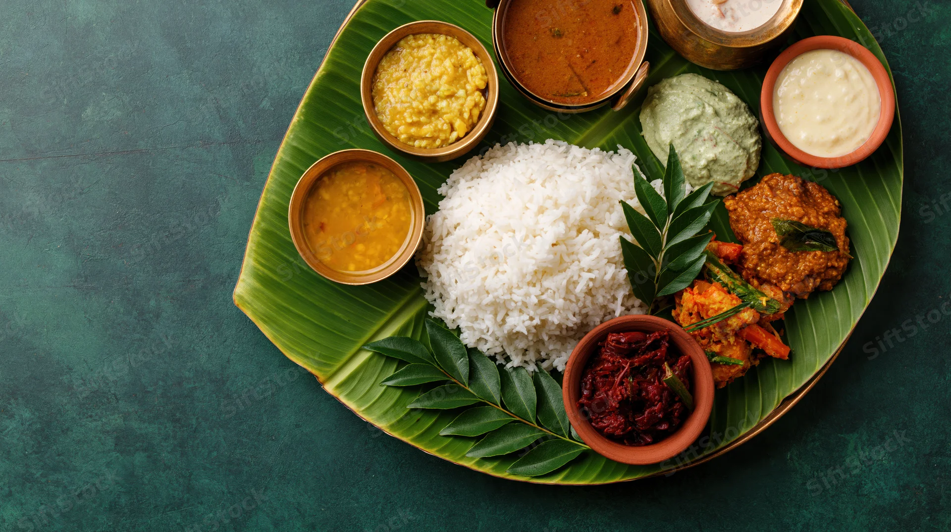 Traditional south indian meal served on banana leaf with rice, curries, chutneys and side dishes arranged overhead