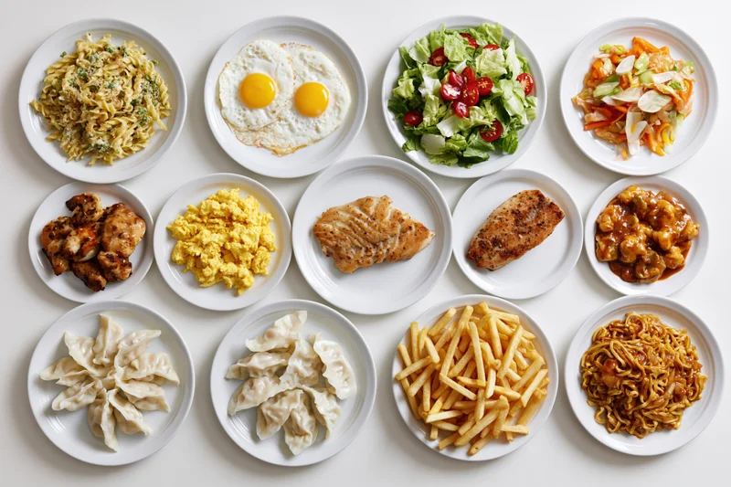 Twelve white plates with different meals arranged in a grid on a white surface