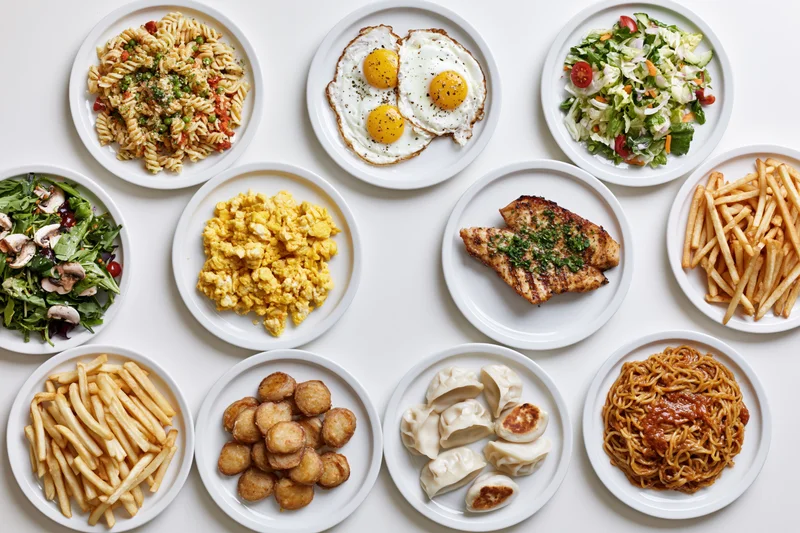Twelve white plates with various meals arranged in grid on white surface