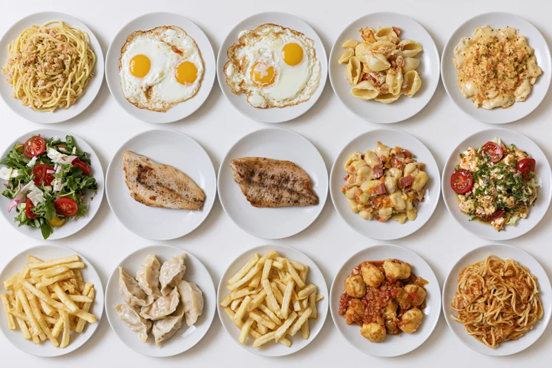 Twelve white plates each holding a different dish arranged in a grid on a white surface