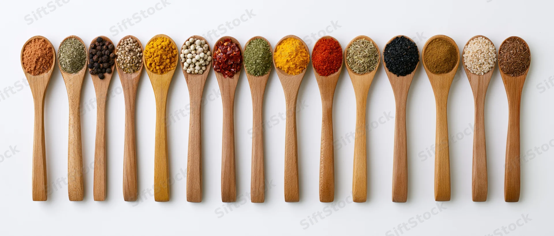 Wooden spoons each holding a different spice arranged in a horizontal row on a white background