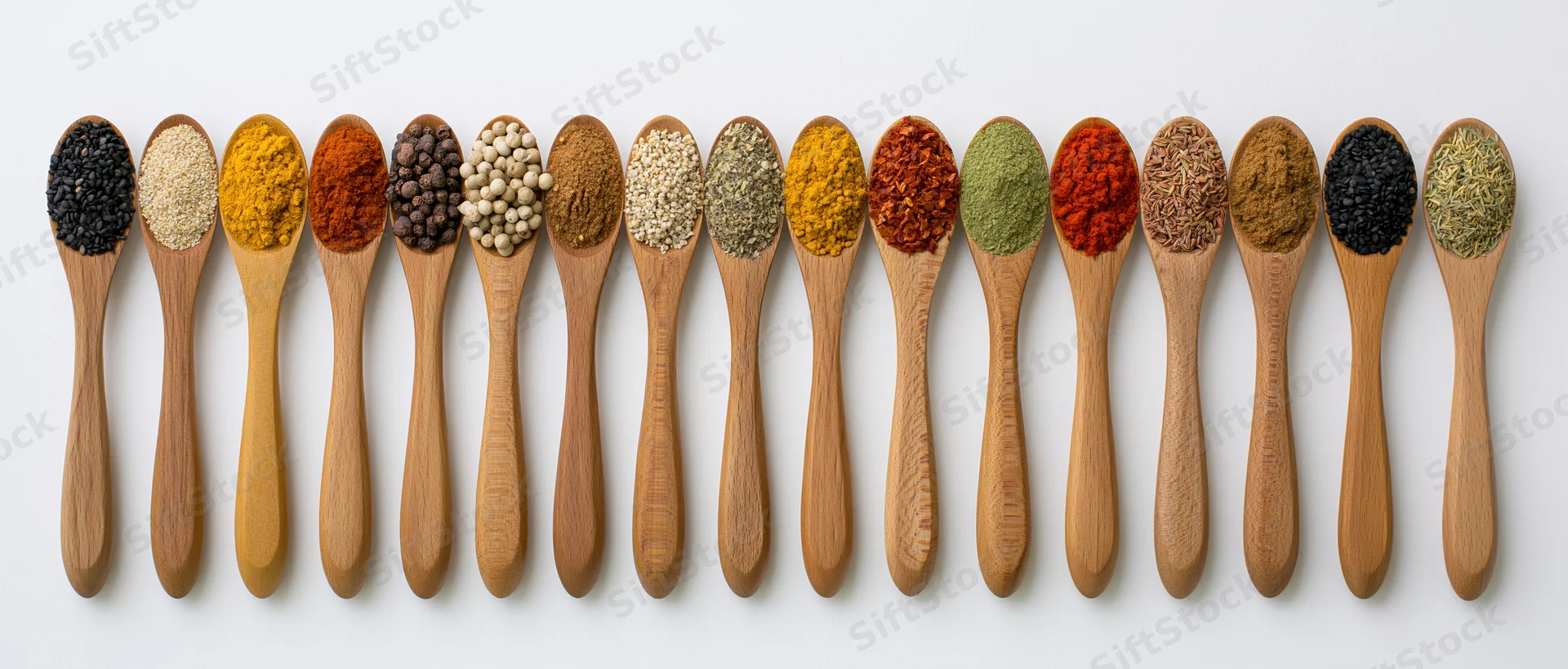 Wooden spoons filled with various spices arranged in a row on white background