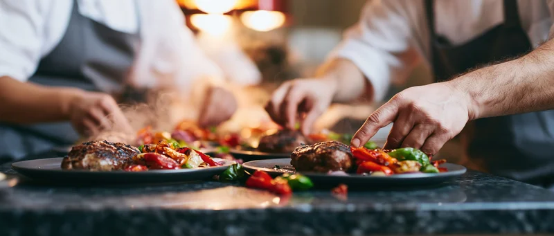 Chefs plating meals with vegetables and steak in a busy restaurant kitchen