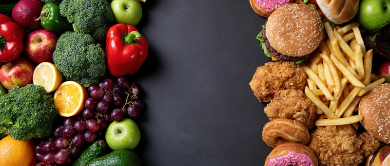 Healthy fruits and vegetables on one side, unhealthy fast food on the other, arranged as side borders on a dark surface