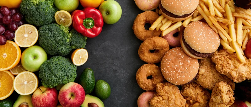Healthy fruits and vegetables contrasted with unhealthy fast food on dark surface