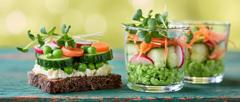 Two spring vegetable arrangements on rye crispbread and in glass jars on a wooden table