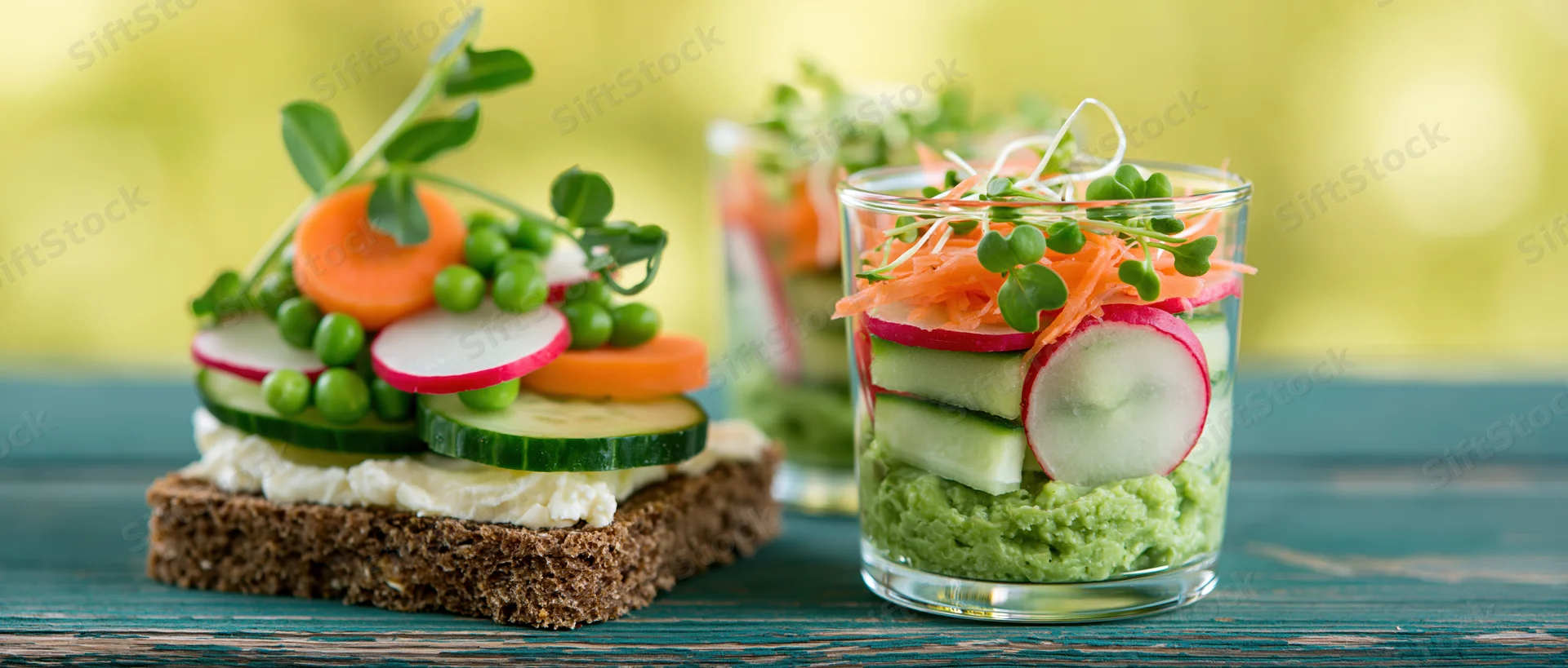 Fresh spring vegetables arranged on rye crispbread and in glass jars on a wooden table