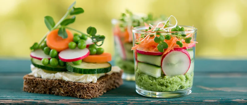 Fresh spring vegetables arranged on rye crispbread and in glass jars on a wooden table