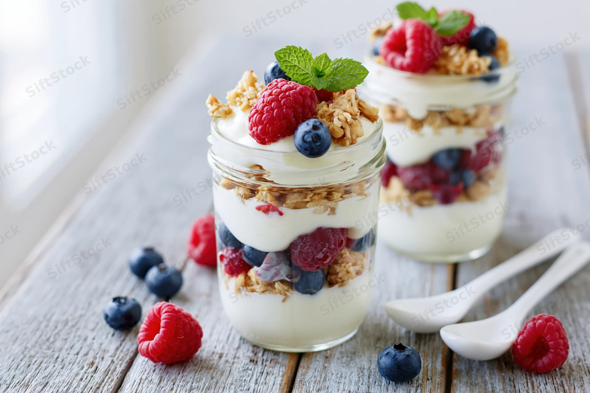 Two glass jars filled with layered yogurt parfait topped with berries and granola on a wooden table