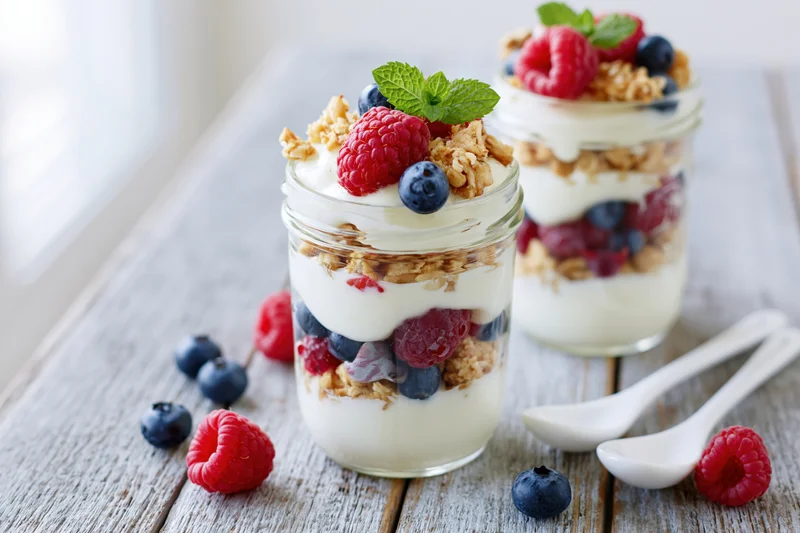 Two glass jars filled with layered yogurt parfait topped with berries and granola on a wooden table