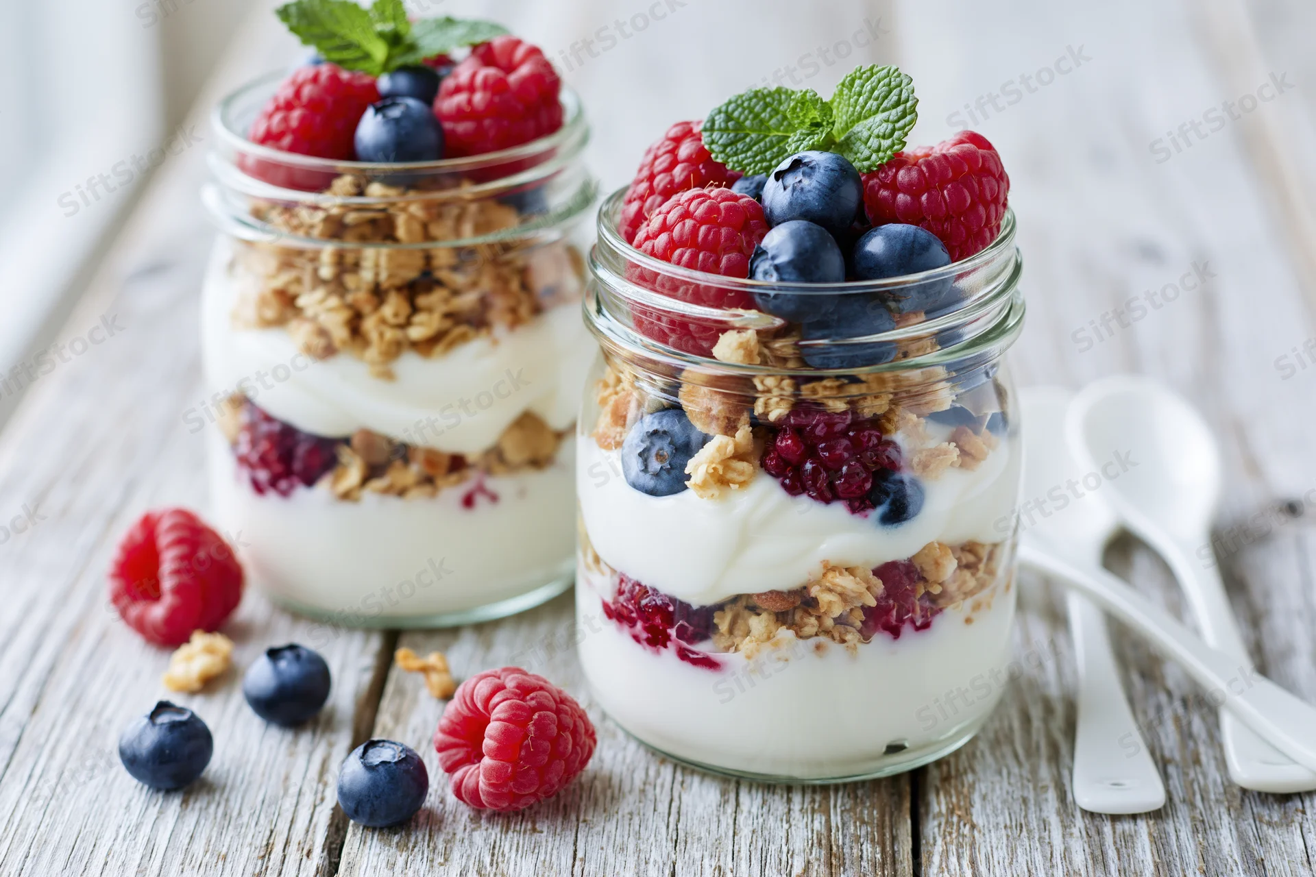 Two glass jars filled with layered yogurt parfait topped with granola and berries on a wooden table