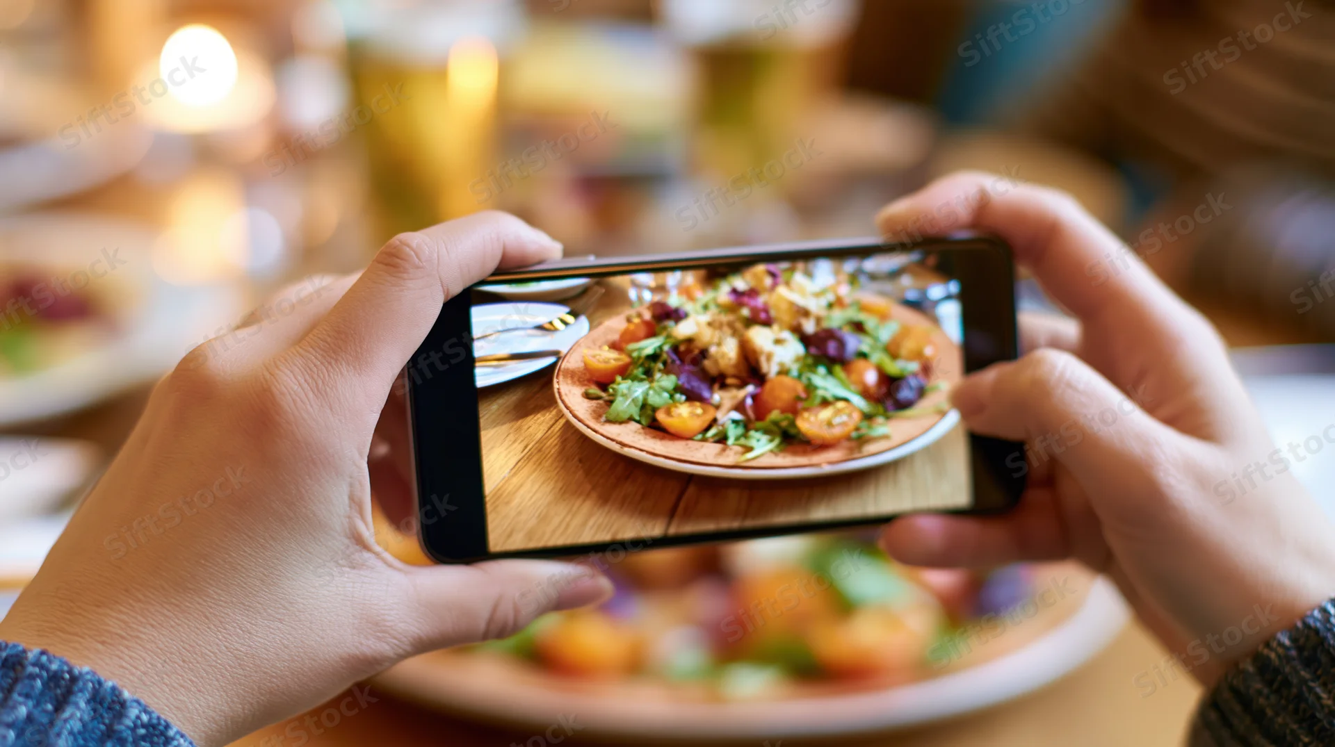 Hands holding smartphone horizontally photographing a salad on a plate at a restaurant table